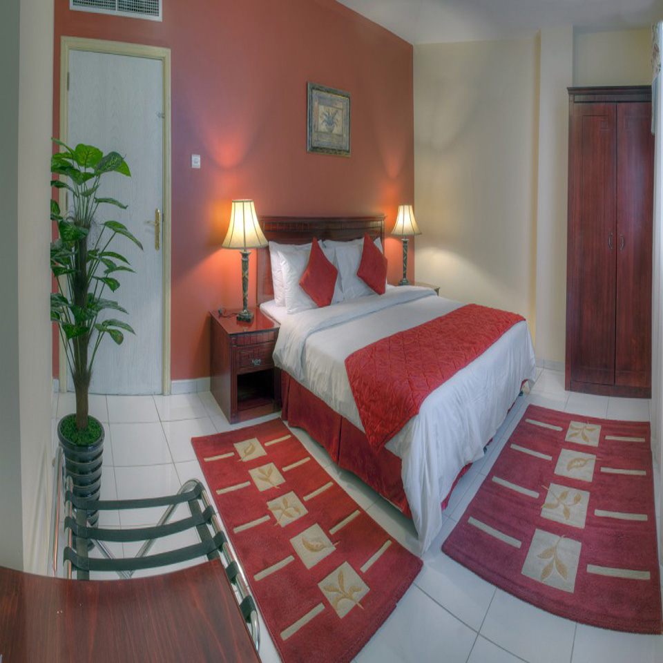 A one-bedroom suite at Al Maha Regency with a king bed and warm terracotta walls